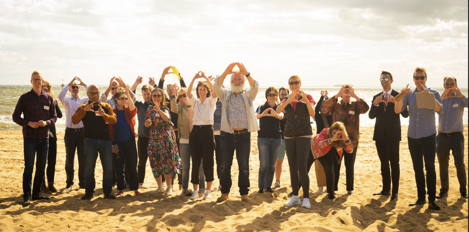 A picture on the beach with lots of people holding their hands together to make a doughnut shape