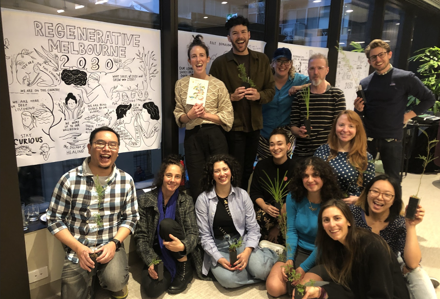 A group of people next to a sign saying ‘Regenerative Melbourne 2030’ holding small plants